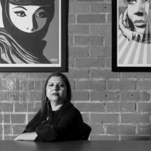 VALOR’s CEO, Sandra Henriquez, sitting at a table and looking towards the camera. Valor U.S. Advancing equity. Ending sexual violence.