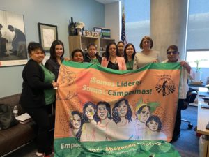 Lideres Campesinas members standing with Assemblymember Aguiar-Curry holding a Lideres Campesinas flag.