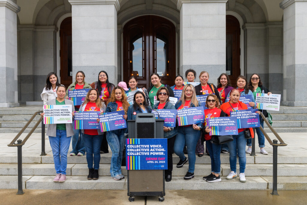Ya Basta Women y Sandra Henriquez sosteniendo carteles para el Día del Denim en las escaleras del Capitolio de California