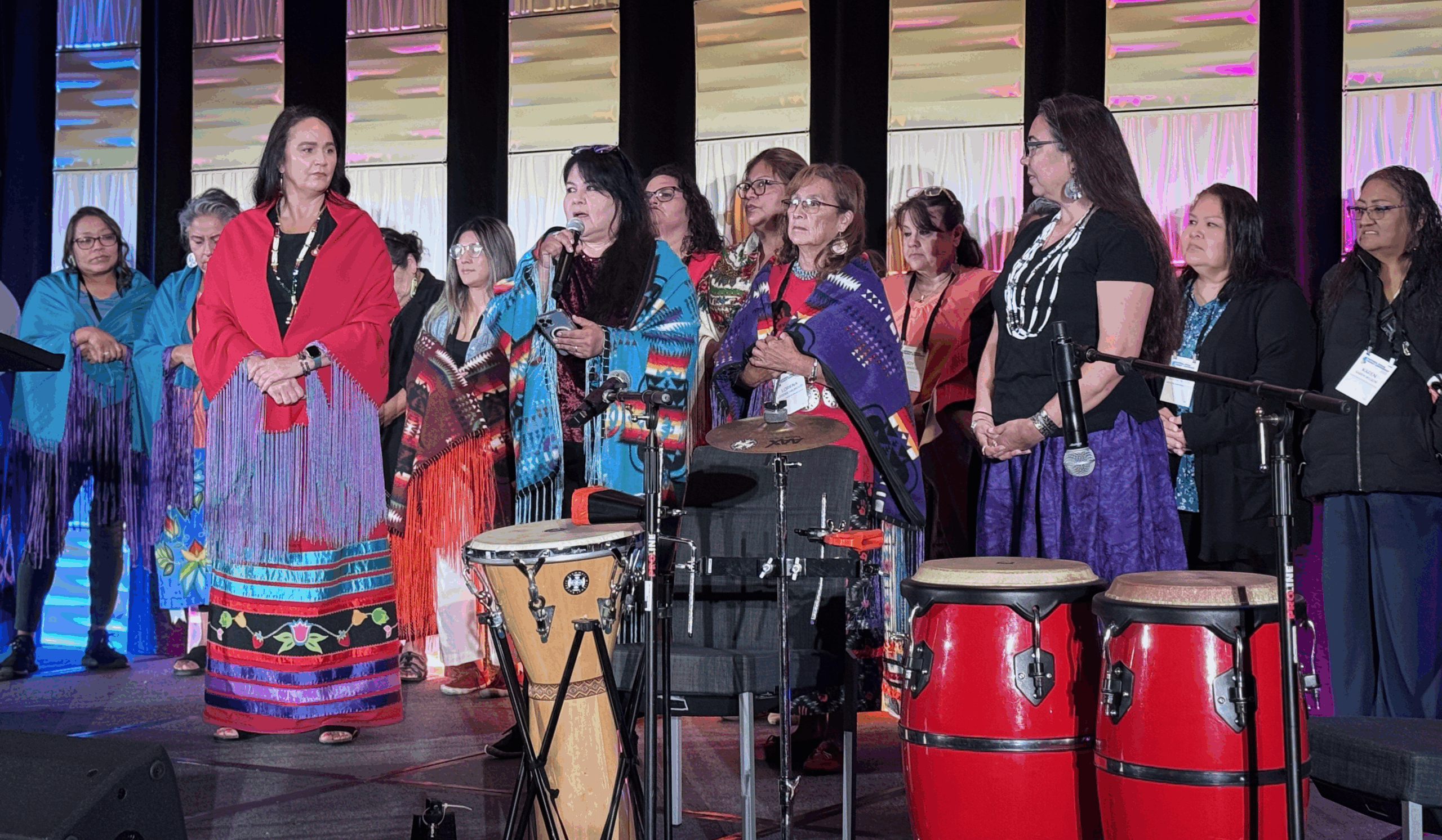 Photo of a group of people wearing bright colors and shawls on stage.
